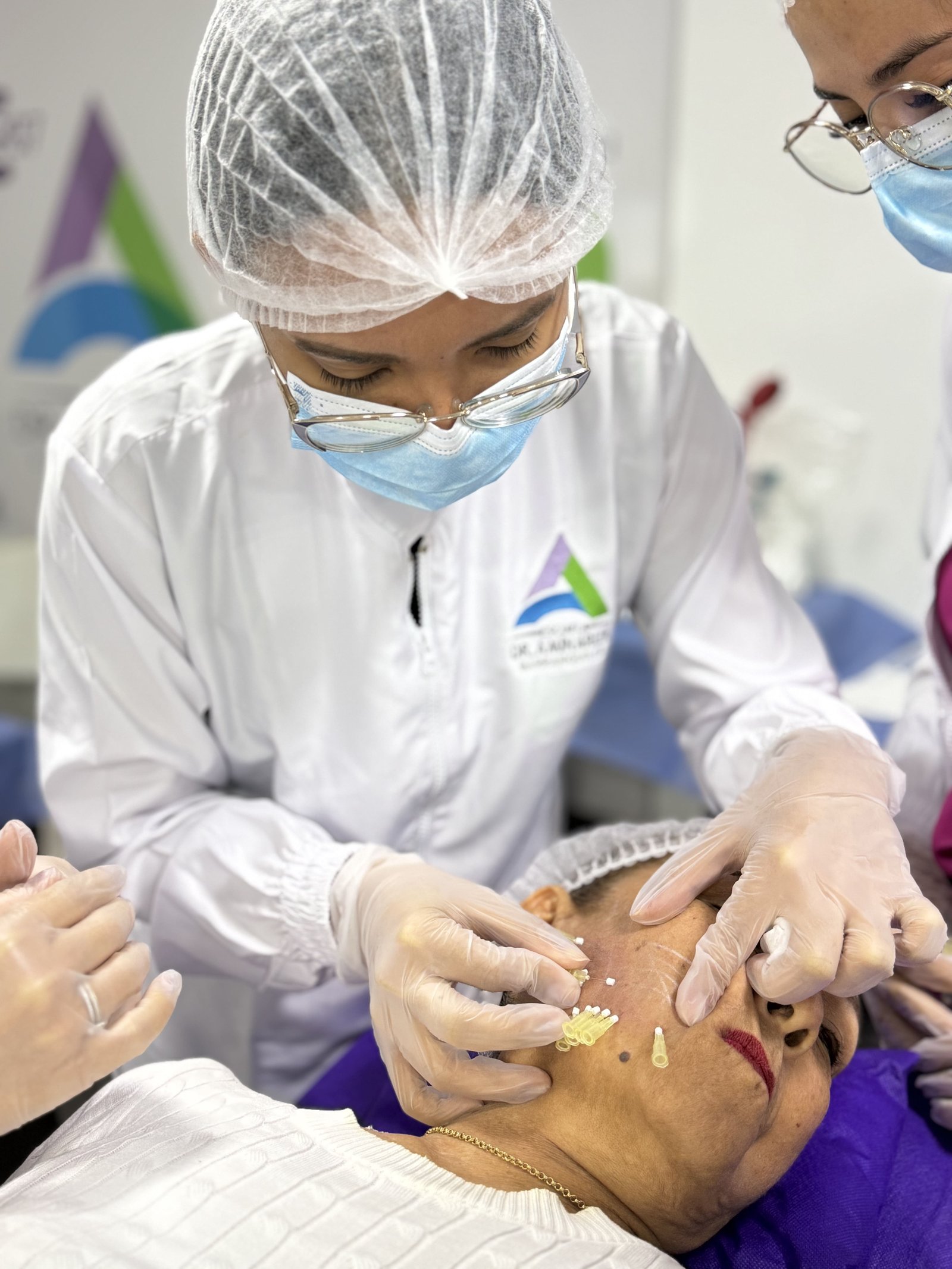 Médica realizando aplicación facial supervisada por docente durante práctica presencial
